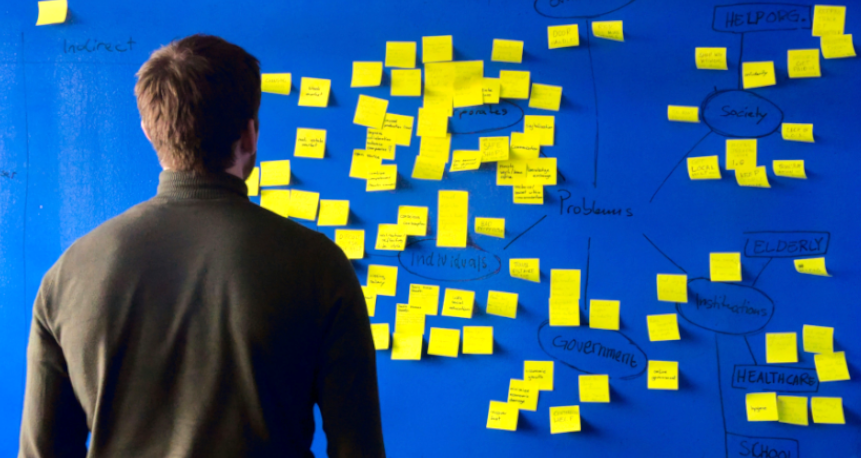 Mann vor Pinnwand mit vielen gelben Post-it Fragen